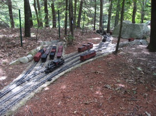 According to the flyer: Scale: Fn3 (1:20.3 3ft narrow gauge) Size: 200 ft x 180 ft, 12 scale miles of track Prototype: American 3 ft narrow gauge Local: rugged hills of the North East Era: 1940-1950s Style: linear with 4 main destinations yards, 8 branch lines, 10 major industries, and 14 additional switching locations Mainline run: 4 scale miles (1000 ft) Minimum degree of curve: 43° (2 Meters) Minimum Turnout: #6 for mainlines #4 for yards/Industries Maximum Grade: 2% mainline, 4% branch Elevation Change: 250 scale ft (13 feet) Roadbed: gravel roadbed Track: 110 lb rail (code 332 stainless steel and brass) 